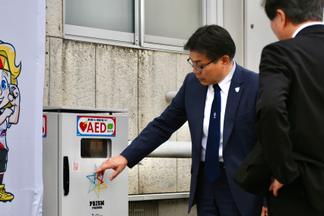 医学部総合グラウンドに設置されたAEDについて説明する村上氏