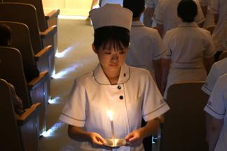 ナイチンゲール像からキャンドルの灯を受ける学生